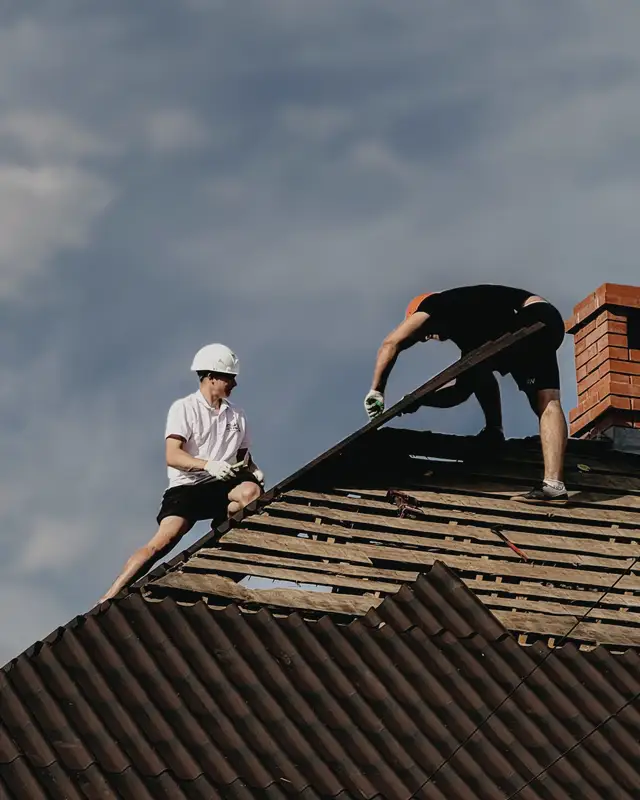 Two roofers repairing a roof under a clear sky